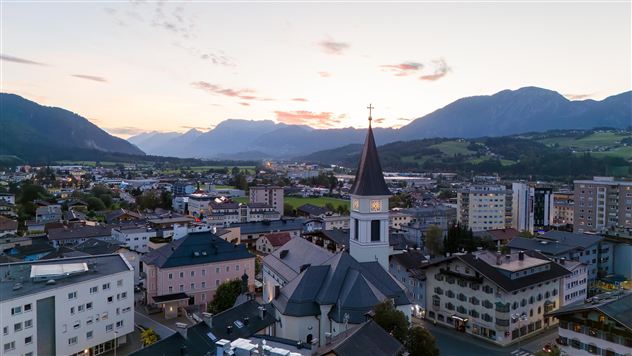 En malerisk by med en kirke i forgrunden og bjerge i baggrunden. himlen er let farvet ved solnedgang.