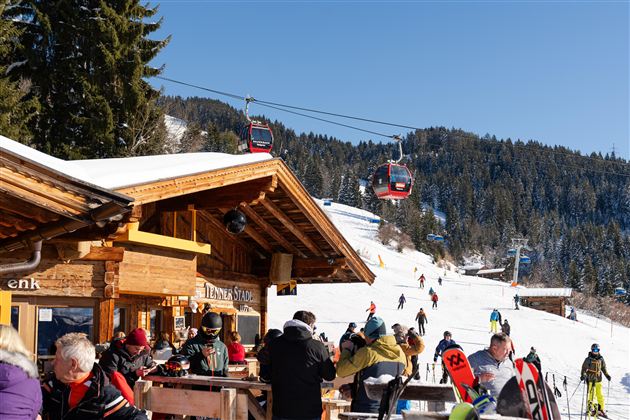 A lively ski resort with a restaurant in the foreground. In the background, skiers are skiing and a gondola hovers over the snowy slopes.