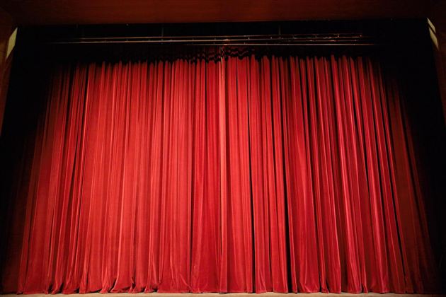 An empty theater hall with red seats and a golden curtain. The light illuminates the curtain in warm tones.