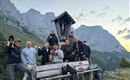 Eine Gruppe von zehn Personen steht fröhlich auf einem Berg. Im Hintergrund sind beeindruckende Felsen und ein klarer Himmel zu sehen.