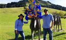 Ein Paar steht neben einer Skulptur einer Kuh, die mit bunten Blumen geschmückt ist. Im Hintergrund sind sanfte Hügel und eine klare Himmel zu sehen.