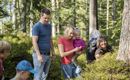 Eine Gruppe von Menschen erkundet den Wald. Einige Kinder und Erwachsene lachen und genießen die Natur.