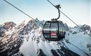 Eine Seilbahn schwebt über schneebedeckte Berge. Der Himmel ist klar und die Landschaft wirkt majestätisch.