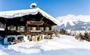 A beautiful chalet in the snow with a snow-covered roof. In the background, impressive mountains can be seen.