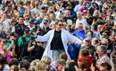 Ein Mann in einem weißen Laborkittel steht im Mittelpunkt einer großen Menschenmenge. Die Zuschauer applaudieren und nehmen Fotos auf.