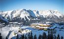 A beautiful snowy landscape with mountains in the background. Skiers and a mountain station can be seen in the foreground.