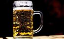 En ølkrus lavet af glas med skummende øl. Kruset står på en træoverflade.