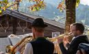 Eine Person spielt auf einem Akkordeon, während sie traditionelle bayerische Tracht trägt. Im Hintergrund sind weitere Musiker zu sehen.