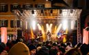 Een liveband speelt op een podium voor enthousiast publiek. De sfeer is feestelijk met lichten en een levendige achtergrond.