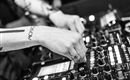 Ein DJ steht am Mischpult und steuert die Musik. Die Hände sind aktiv und fokussiert auf die Regler.