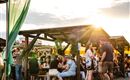 Ein belebter Markt mit vielen Menschen, die an Tischen sitzen und essen. Die Sonne scheint und sorgt für eine angenehme Atmosphäre.