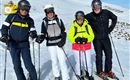 Eine Gruppe von vier Skifahrern steht auf einer verschneiten Piste. Der Himmel ist klar und blau.