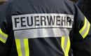 Ein Feuerwehrmann in Uniform. Auf der Jacke steht "FEUERWEHR" in großen Buchstaben.