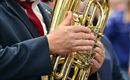 Hudebník drží lesklou tubu v ruce. Zaměřeno je na zlatý nástroj a ruce hráče.