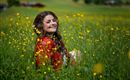 Eine lächelnde Frau sitzt in einem blühenden Feld mit gelben Blumen. Sie trägt ein rotes Kleid und genießt die Natur.