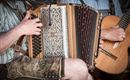 Ein Musiker spielt auf einem Akkordeon, während ein anderer Musiker eine Gitarre hält. Beide tragen traditionelle Kleidung.