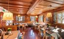 Eine Gruppe von Musikern spielt auf einer Terrasse vor einem traditionellen bayerischen Gasthaus. Sie tragen typische Trachten und haben verschiedene Instrumente dabei.