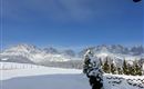 Eine schneebedeckte Landschaft mit majestätischen Bergen im Hintergrund. Der Himmel ist klar und strahlend blau.