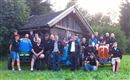 Eine Gruppe von Menschen steht vor einer alten Scheune mit Traktoren. Alle tragen schwarze T-Shirts und lächeln in die Kamera.