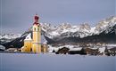 Eine bunte Kirche steht in einer verschneiten Landschaft. Im Hintergrund erheben sich majestätische Berge.