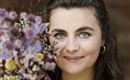 A woman holds a colorful bouquet of flowers and smiles. Her gaze is friendly and her eyes shine.