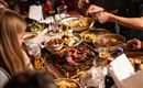 Ein gemütliches Essen mit Freunden, das verschiedene Gerichte und Getränke umfasst. Auf dem Tisch liegen Fleisch, Beilagen und Salat.