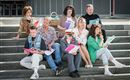 A group of people is sitting on steps and holding various documents in their hands. They seem to be rehearsing a performance or a casting.
