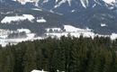 A cozy mountain cabin in the snow surrounded by fir trees and majestic mountains. The sky is cloudy and the landscape appears peaceful.