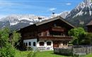 A traditional farmhouse in the mountains with snow-covered peaks in the background. The surroundings are green and inviting, ideal for rural recreation.