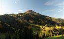 Zwei Radfahrer stehen auf einer Wiese und blicken auf eine wunderschöne Berglandschaft. Die Sonne geht gerade unter und schafft eine malerische Atmosphäre.