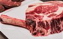 Ein großes, rohes Tomahawk-Steak auf einem weißen Teller. Das Fleisch hat eine ausgeprägte Marmorierung und einen langen Knochenschaft.