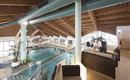 Ein moderner Wellnessbereich mit einem großen Pool und gemütlichen Sitzgelegenheiten. Pflanzen und Holzdetails schaffen eine entspannte Atmosphäre.