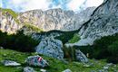 Eine beeindruckende Berglandschaft mit hohen Felsen und einer grünen Wiese. Am Hang sind Wanderzeichen sichtbar.