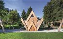 A modern wooden playground with a striking triangular playhouse. In the background, trees and swings can be seen.
