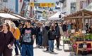 Ein belebter Markt mit vielen Menschen, die entlang der Stände schlendern. Die Atmosphäre ist freundlich und lebhaft.