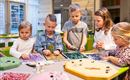 A group of children is working together on a craft project. They are sorting colorful beads and gems on a table.
