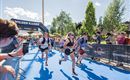 A group of runners reaches the finish line in a race.  
Spectators stand along the course and cheer on the participants.