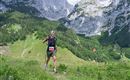 A runner wanders happily in a picturesque mountain landscape. High mountains and green meadows surround him.