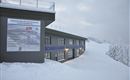 Ein modernes Gebäude in einer verschneiten Landschaft. Schilder mit technischen Informationen zur Schneeproduktion sind sichtbar.