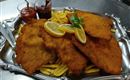 Ein großer Teller mit knusprigem Schnitzel, serviert mit Pommes frites und zwei verschiedenen Dips. Frische Zitronenscheiben und ein Minzblatt verleihen dem Gericht eine dekorative Note.