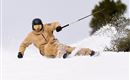 A skier is skiing in a snowy area. He is wearing a beige ski jacket and a helmet.