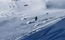 Ein Skifahrer fährt auf unberührtem Schnee in einer Berglandschaft. Die Spuren im Schnee zeigen die Abfahrt und verleihen der Szene Dynamik.