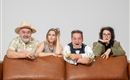 Eine Gruppe von vier Personen sitzt auf einer Couch. Sie zeigen verschiedene Gesichtsausdrücke und wirken unterhaltsam und gespannt.