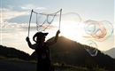 Eine Person steht im Sonnenuntergang und bläst Seifenblasen. Die Berge und der Himmel sind im Hintergrund gut sichtbar.