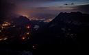 A breathtaking mountain landscape at night with glowing city lights in the valley. The sky displays soft hues of twilight.