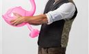 A cheerful man is wearing traditional attire and holding an inflatable flamingo toy. He is smiling and posing against a neutral background.
