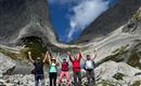 Eine Gruppe von fünf Wanderern steht inmitten einer malerischen Berglandschaft. Sie feiern ihren Erfolg, indem sie die Hände in die Luft heben.