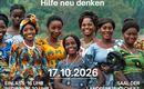 Eine Gruppe von Frauen in bunten traditionellen Kleidern steht fröhlich zusammen in einer grünen Umgebung. Der Text auf dem Bild kündigt eine Veranstaltung zur Unterstützung von TSHUMBE an.