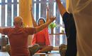 Eine Gruppe von Menschen praktiziert Yoga in einem hellen Raum. Die Atmosphäre ist ruhig und entspannt, mit Holzwänden und natürlichem Licht.