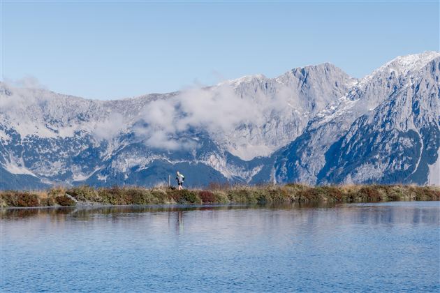 Ein stiller See umgeben von majestätischen Bergen und Wolken. Die Landschaft strahlt Ruhe und natürliche Schönheit aus.